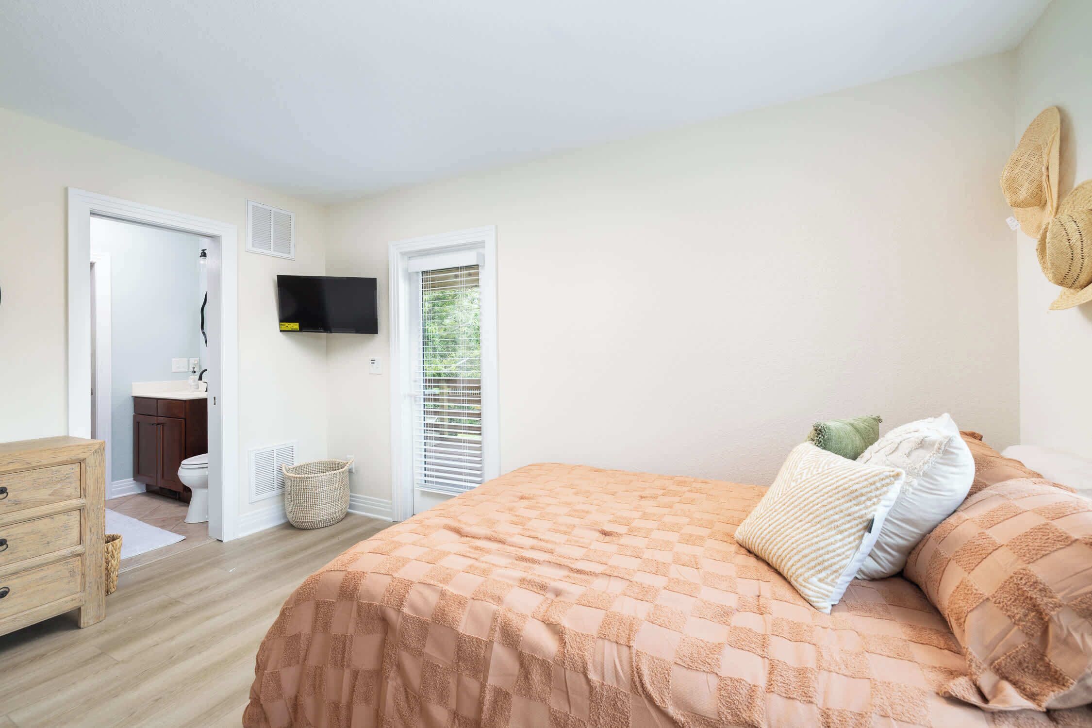Ein Schlafzimmer mit Bett, Kommode, Fernseher und einem durchgehenden Türrahmen sichtbaren Badezimmer.