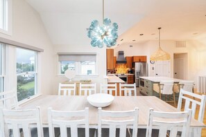 A modern kitchen with white cabinetry, a large island, and a dining area with a wooden table and white chairs. - Duck Resort with Ocean Views, Pool, HotTub, Elevator (Kitty Hawk)