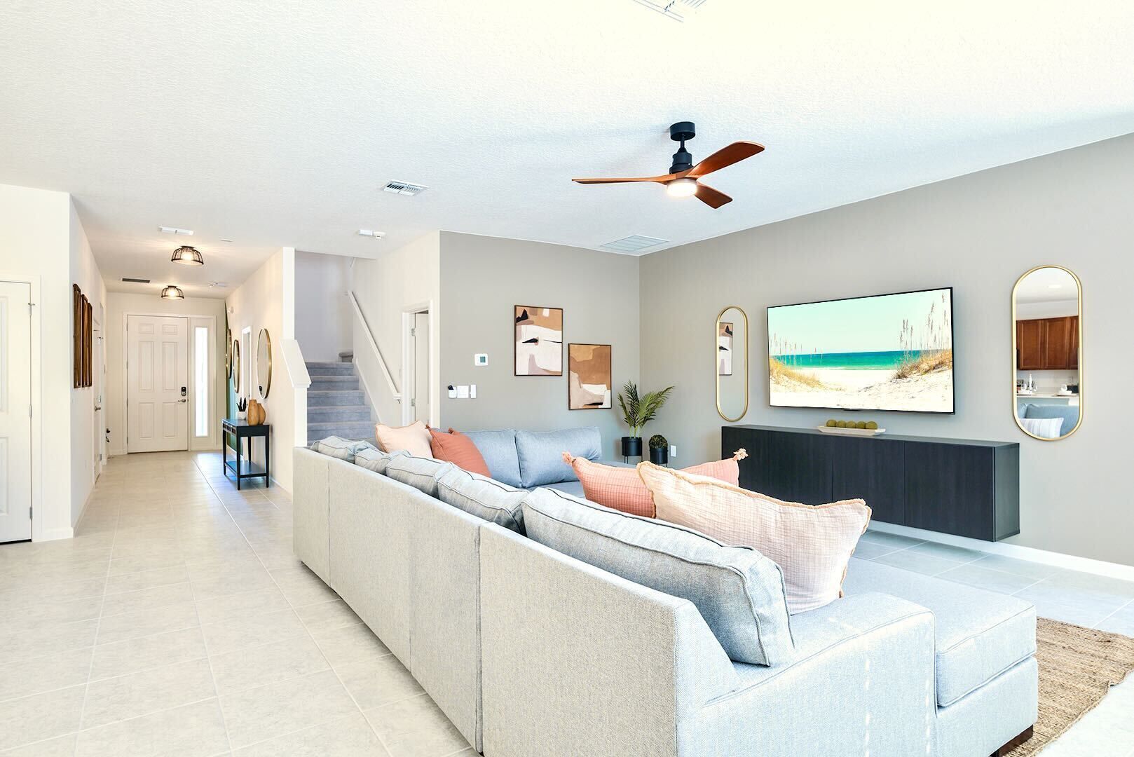 A modern living room with a large sectional sofa, a flat-screen TV, and a ceiling fan.