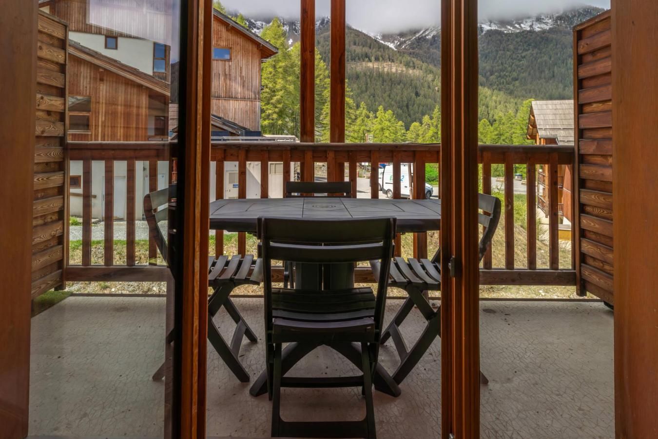 A wooden deck with a table and chairs, overlooking a mountainous landscape.