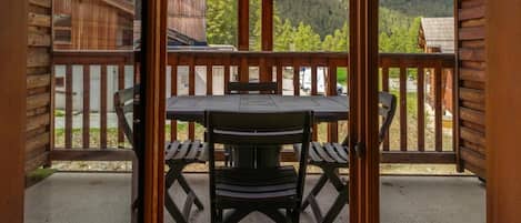 A wooden deck with a table and chairs, overlooking a mountainous landscape.