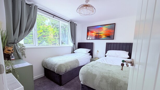 A bedroom with two beds, a window with curtains, a radiator, a wall-mounted picture, and a ceiling light fixture. - 2 bedroom full referbished anex, sleeps 4. Kitchen, Cooker, fridge/freezer. (bradford)