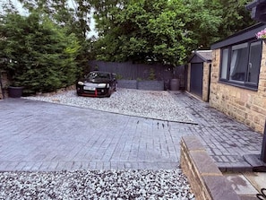 A car parked in a driveway with gravel, a wooden fence, and a building with a window.