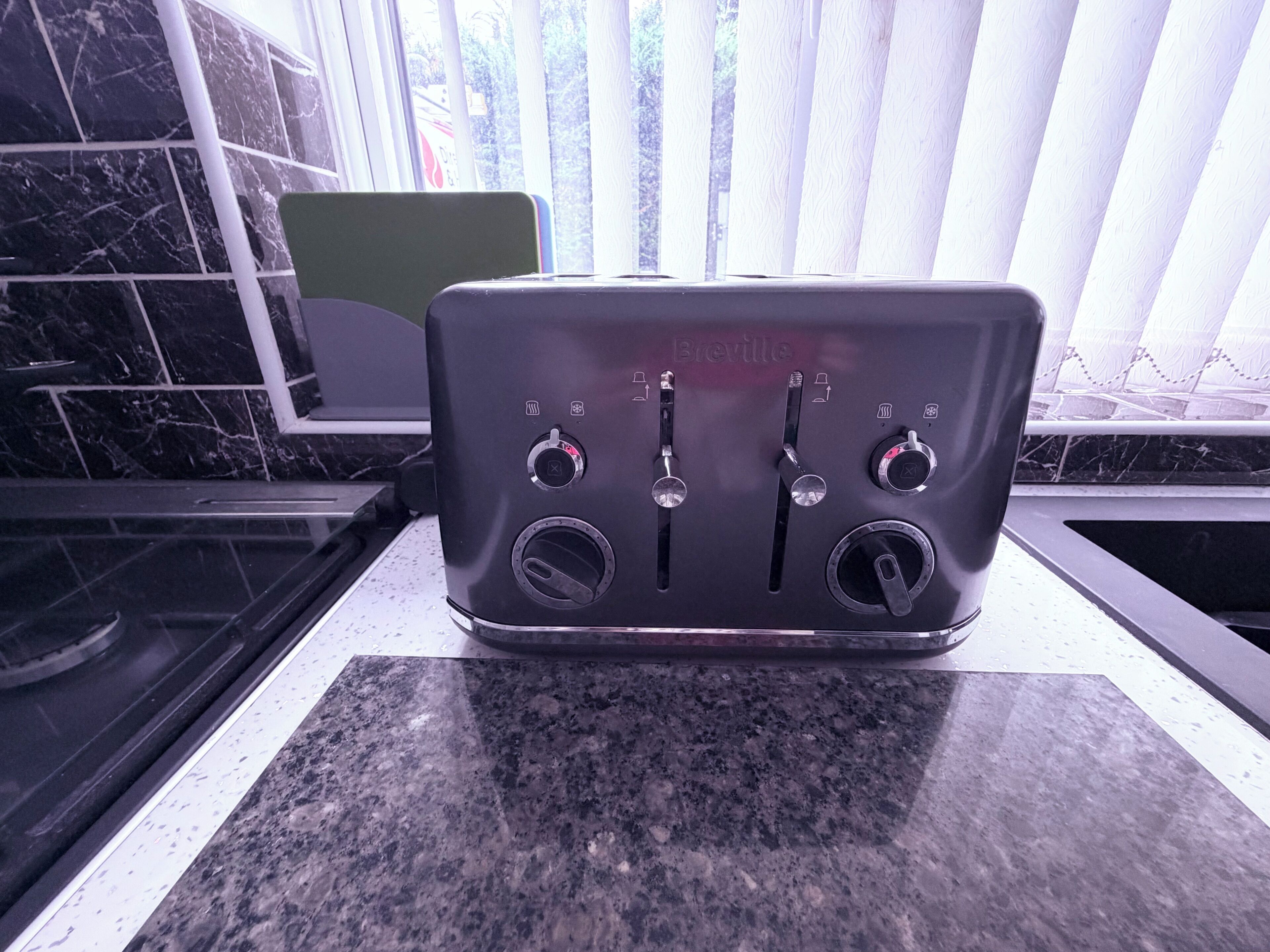 Ein Breville-Toaster steht auf einer Granitabdeckung in einer Küche mit schwarzen Marmorfliesen und einem Fenster mit Jalousien.
