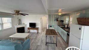 A compact living space with a sofa, television, fireplace, kitchenette, and a ceiling fan.