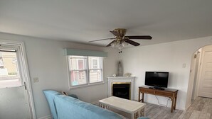 A living room with a sofa, a fireplace, a television, and a ceiling fan.