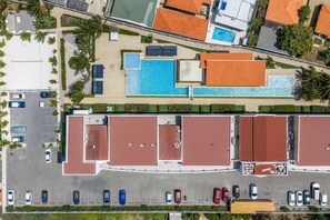 Vista aérea de um hotel com piscina, estacionamento e vários edifícios com telhados vermelhos.