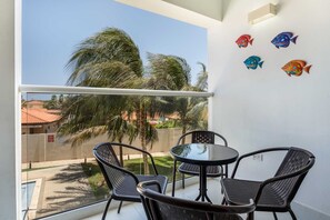 Varanda com mesa e cadeiras, vista para palmeiras e arte de parede com peixes decorativos.