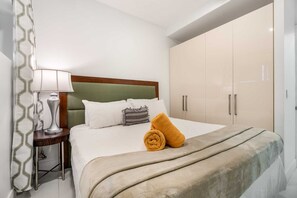 Quarto de hotel com uma cama, mesa de cabeceira, abajur, guarda-roupa e cortina estampada.