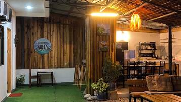 Un intérieur comprenant un espace recouvert d’un gazon synthétique vert, des murs en bois, un coin repas avec des tables et des chaises, et une cuisine à l’arrière-plan.