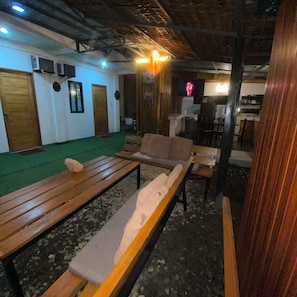A room with wooden benches and a green carpet, a television mounted on the wall, and a wooden door. - Charming 3-bedroom apartment with AC, smart tv , fridge ,wifi, kitchen ,& garage (Elnido)