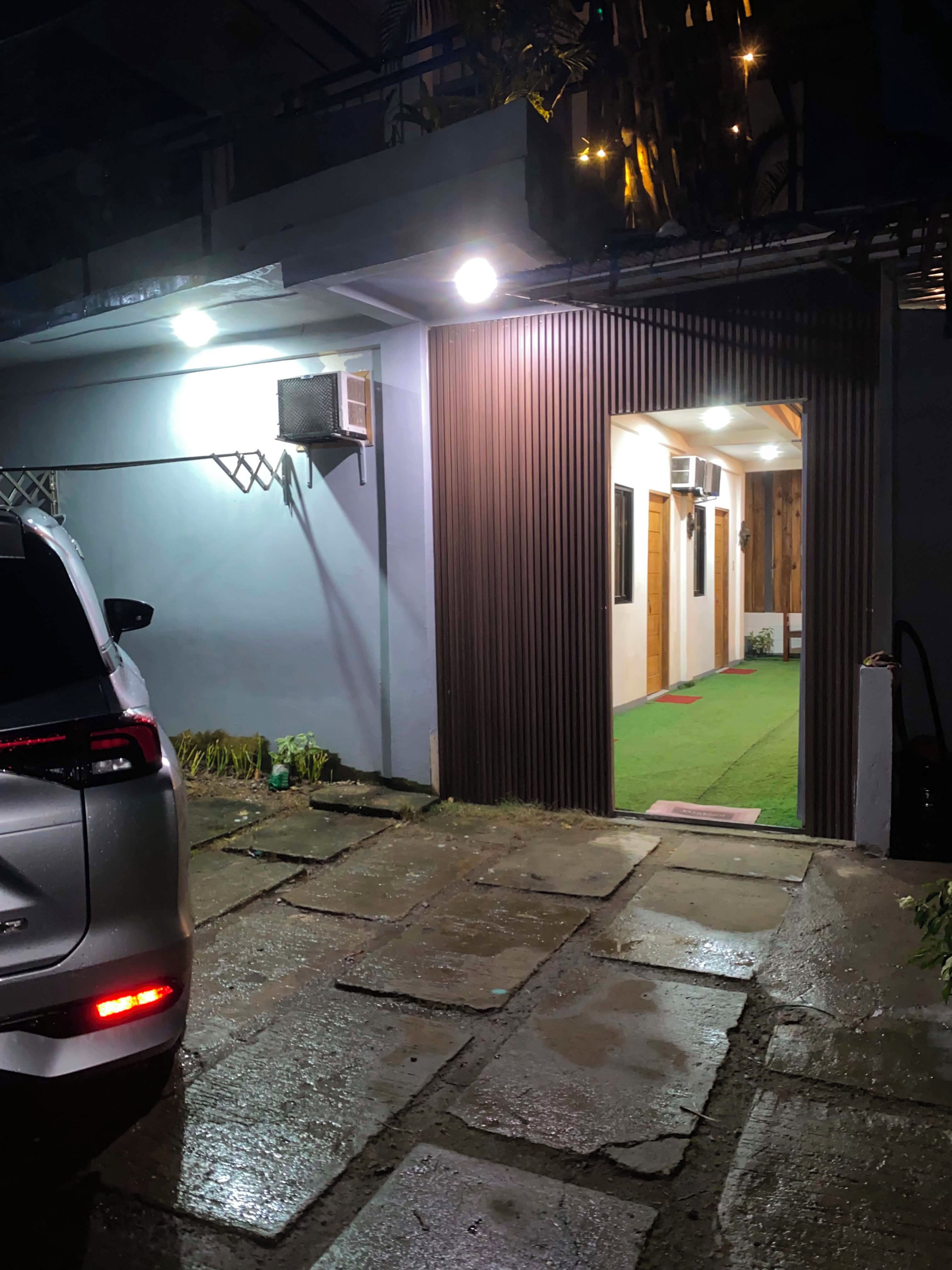 Une entrée fermée par un portail, avec une voiture garée à l’extérieur, un chemin menant à un bâtiment et une pelouse verdoyante visible à travers le portail.