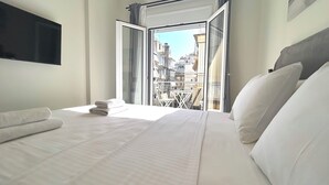 Ett hotellrum med en säng, en tv som är monterad på väggen och utsikt över staden genom en öppen dörr.