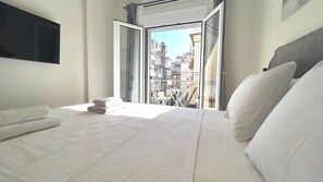A hotel room with a bed, a TV mounted on the wall, and a view of the city through an open door. - Modern Bright 1BR next to Pasalimani & Marina Zeas (Pireas)