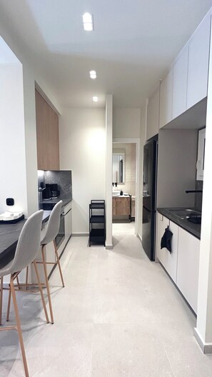 A modern kitchen with a dining area, featuring a countertop, chairs, and a refrigerator. - Modern Bright 1BR next to Pasalimani & Marina Zeas (Pireas)