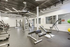 Ein Fitnessraum mit unterschiedlichen Trainingsgeräten, einer zentralen Säule und einem Fenster mit Blick.