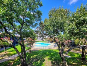 A swimming pool surrounded by trees, a grassy area, and a building in the background. - Sleepover | Alluring Studio + Gym - Austin TX (Austin)