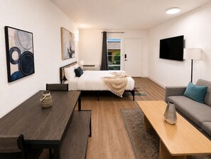 A modern hotel room with a bed, a sofa, a dining table, a TV, and artwork on the walls. - Sleepover | Alluring Studio + Gym - Austin TX (Austin)