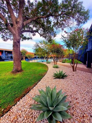 A landscaped outdoor area with a large tree, a pathway, and a building in the background. - Sleepover | Quaint Studio + Gym - Austin TX (Austin)