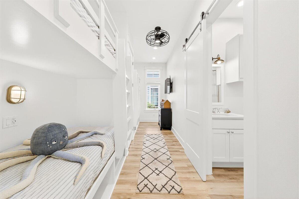 A narrow hallway with a patterned rug, a bed with a unique headboard, a ceiling fan, and a small cabinet.