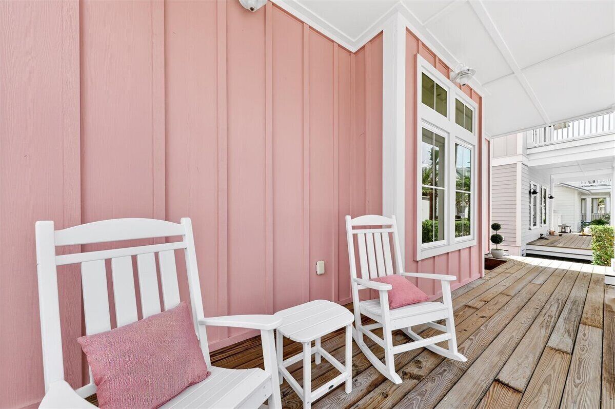Eine Veranda mit zwei weißen Schaukelstühlen, einer mit rosa Kissen, und einem Holzdeck.