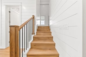 A staircase with wooden steps and black railings, leading to a room with white walls and a window. - Surfside 108 CRE (Port Aransas)