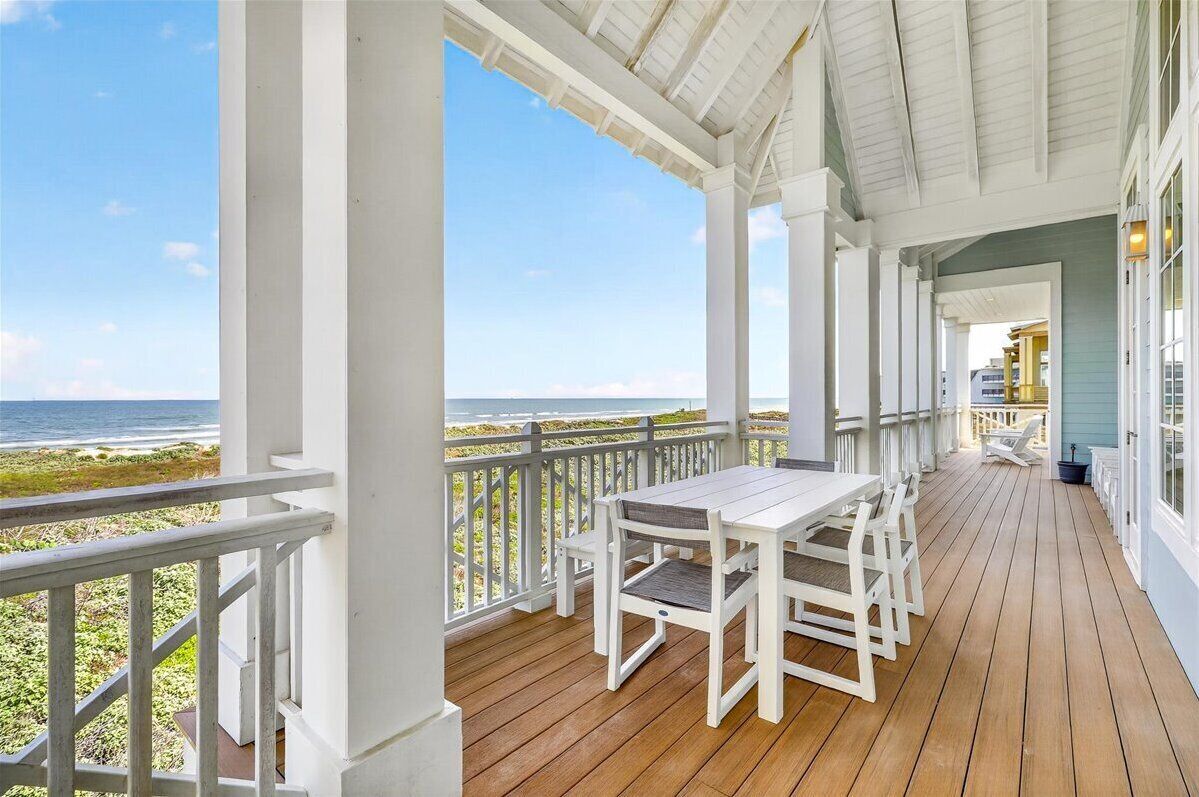 A covered porch with a wooden deck, white railings, and a view of the ocean.