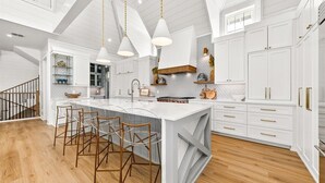 A spacious kitchen with white cabinetry, a large island, and bar stools. - Surfside 108 CRE (Port Aransas)