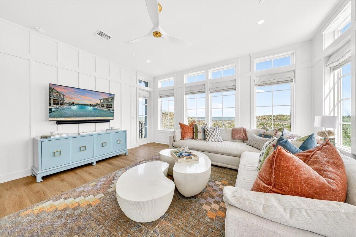 A spacious living room with a large flat-screen TV, a sofa set, a coffee table, and a patterned rug.