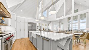 A spacious kitchen with a large island, white cabinetry, and a high ceiling with exposed beams. - Surfside 108 CRE (Port Aransas)