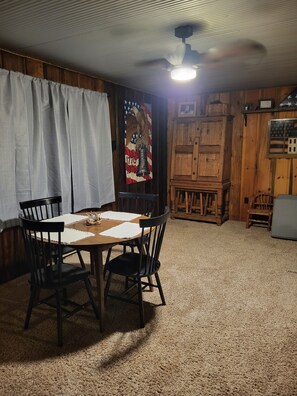 Una habitación con una mesa y sillas de madera, un ventilador de techo y una pared con una bandera y un águila.