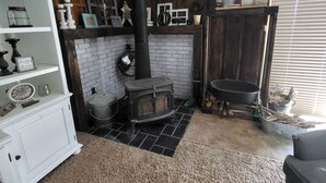 A cozy room with a fireplace, a white brick wall, a wooden shelf with kitchen utensils, a white cabinet, and a black bathtub. - Breathtaking views surrounding this home, perfect for a relaxing getaway! (Cody)