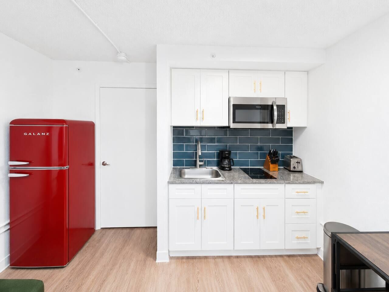 A compact kitchen with white cabinets, a red refrigerator, a microwave, and a coffee maker.