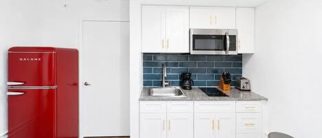 A compact kitchen with white cabinets, a red refrigerator, a microwave, and a coffee maker.