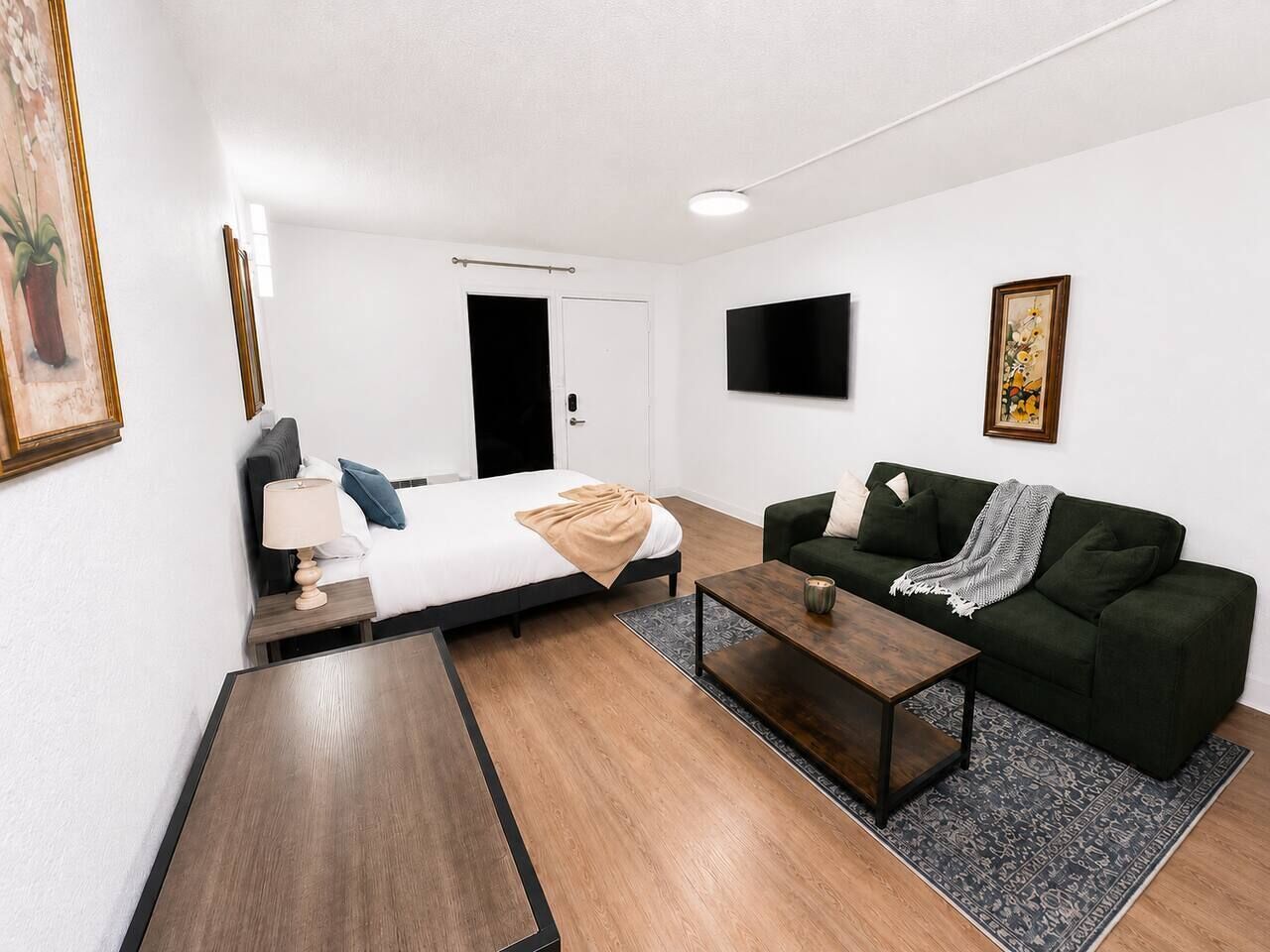 A modern room with a bed, a green sofa, a coffee table, and a TV mounted on the wall.