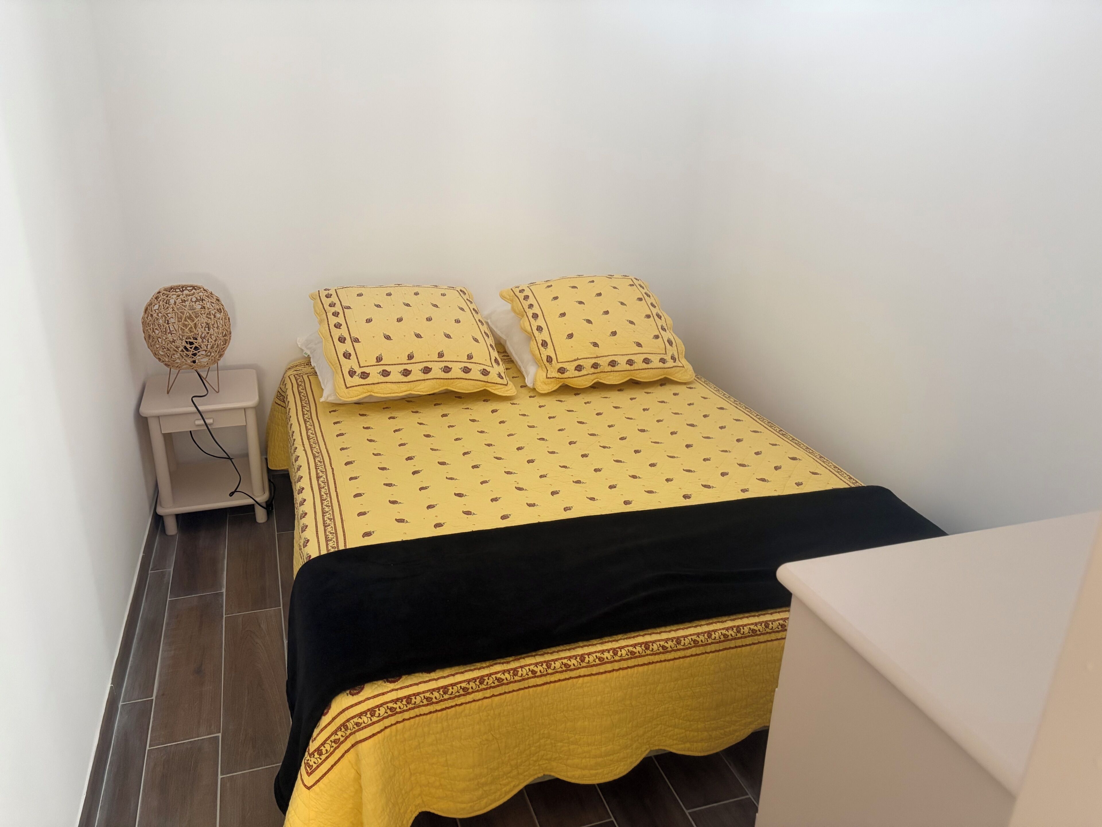A small, neatly arranged bedroom with a bed, pillows, a bedside lamp, and a nightstand.