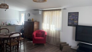 A modern living room with a dining area, a red armchair, a flat-screen TV, wicker pendant lights, and a kitchen in the background. - Getaway in the Baronnies: House with a Terrace (Chaudebonne)