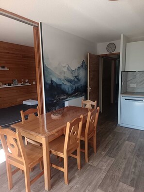 Ein Essbereich mit Holztisch und -stühlen, eine Küche mit Kühlschrank und eine Wand mit einer Berglandschaftsmalerei.