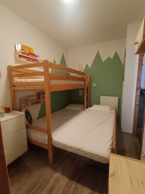 Ein Schlafraum mit Etagenbetten, einem Schreibtisch und Regalen, Wände in Grün mit Berggestalten und ein Holzboden.