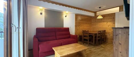 Une pièce avec un plancher en bois, un canapé rouge, une table basse en bois, une table à manger avec des chaises et un panneau mural en bois.