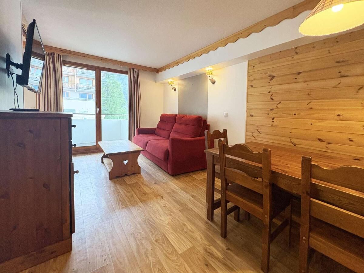 A room with a wooden dining table, a red sofa, a wooden cabinet, and a small table with a heart-shaped design.