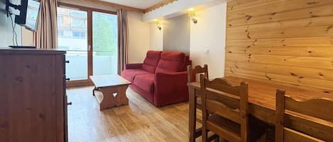 A room with a wooden dining table, a red sofa, a wooden cabinet, and a small table with a heart-shaped design.