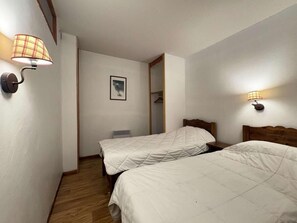 A hotel room with two beds, a wooden floor, a white wall, and a door leading to a bathroom. - Ski-in/ski-out & foot of the slopes, Ground floor, swimming pool, sauna, balcony, tv, ski locker (Les Orres)