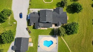 Eine Vogelperspektive zeigt ein Wohnanwesen mit Schwimmbad, Auffahrt und einem großen Haus mit mehreren Dächern.