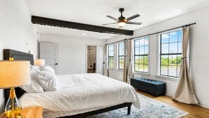 Ein Schlafzimmer mit Bett, Nachttischlampe, Fenster und Deckenventilator.