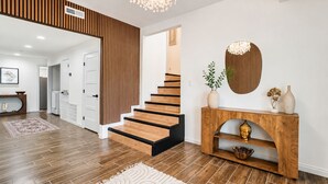 Ein modernes Interieur mit einer Holztreppe, einem Konsolentisch mit Dekoration und einem großen Spiegel.