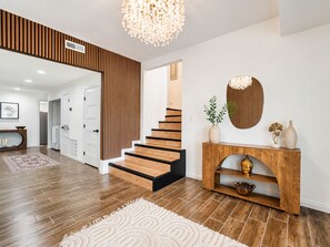 Ein modernes Interieur mit einer Holztreppe, einem Konsolentisch mit Dekoration und einem großen Spiegel.