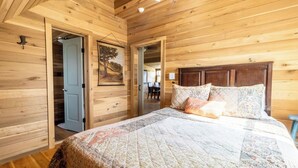 Quarto com painéis de madeira, uma cama, uma porta que dá para outro espaço e um quadro na parede.