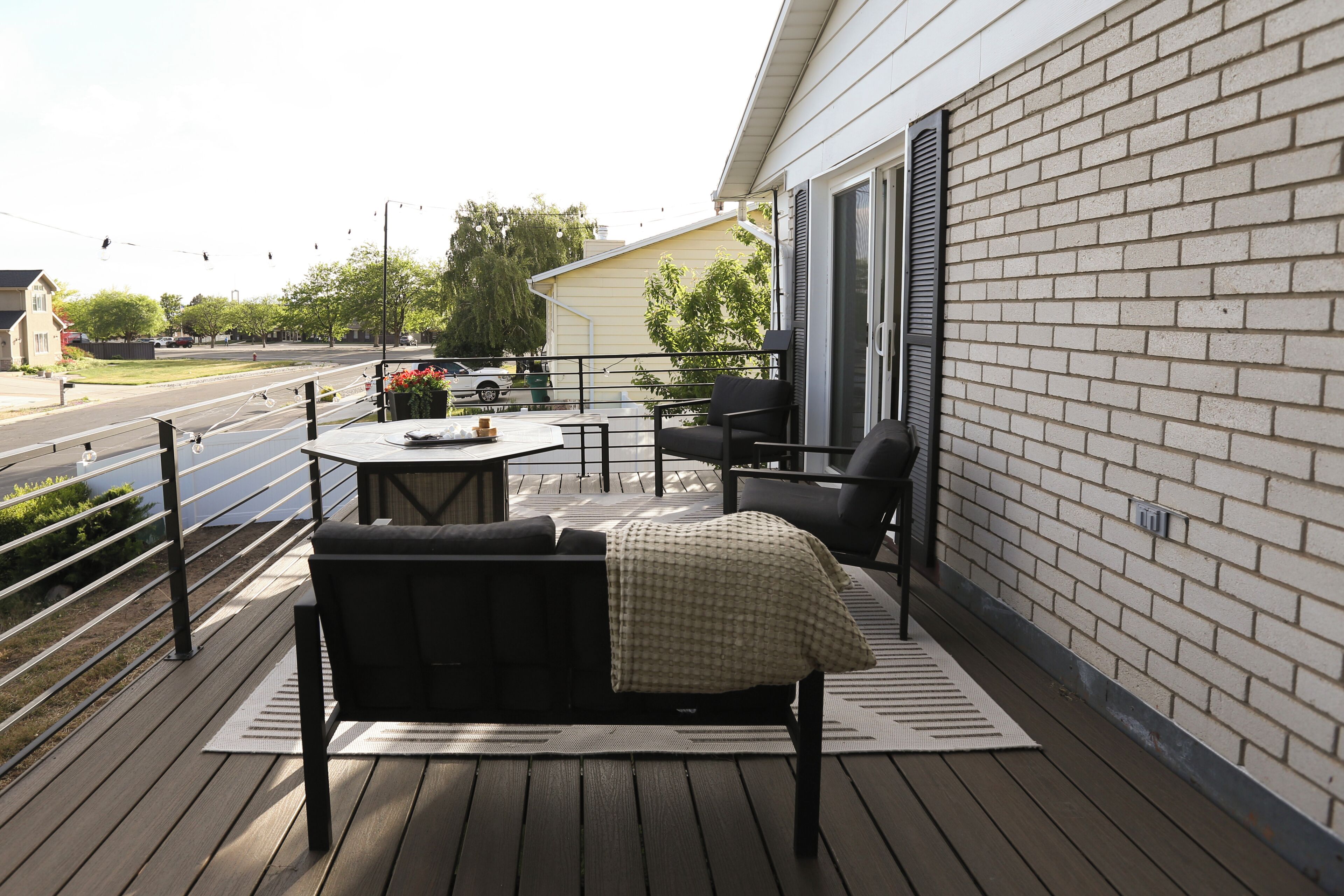 A deck with a sofa and chairs, a table, and a view of the street.