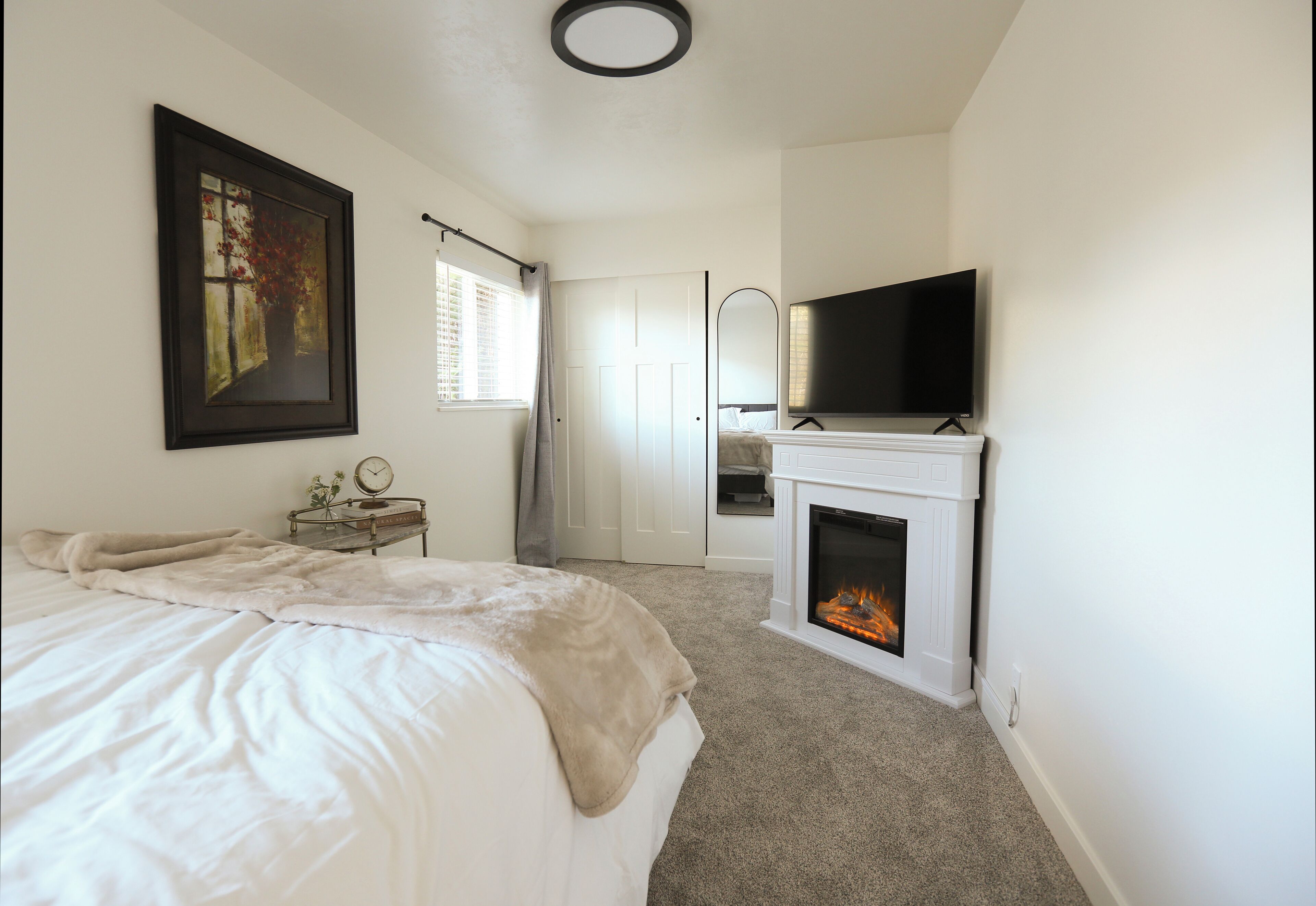 A bedroom with a bed, a fireplace, a television, and a door leading to another room.